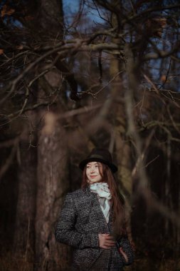 Genç bir kadın, güneşli bir günde sonbahar Ormanda yürür. Bir kız bir palto ve şapka ağaçların dallarında portresi