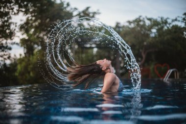 Açık Yüzme havuzunda genç kadın saç spreyi yapar.