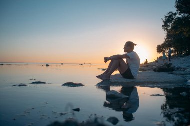 Genç bir adam bir taş denizin kenarında oturur. 