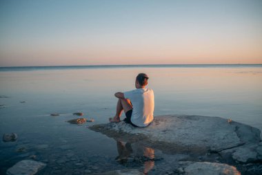 Genç bir adam bir taş denizin kenarında oturur. 