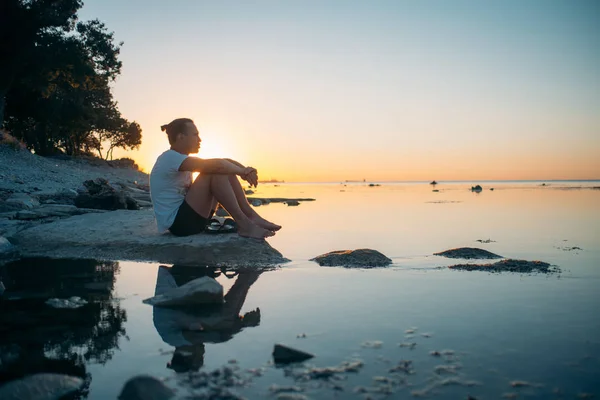 En ung man sitter på en sten vid havet. — Stockfoto