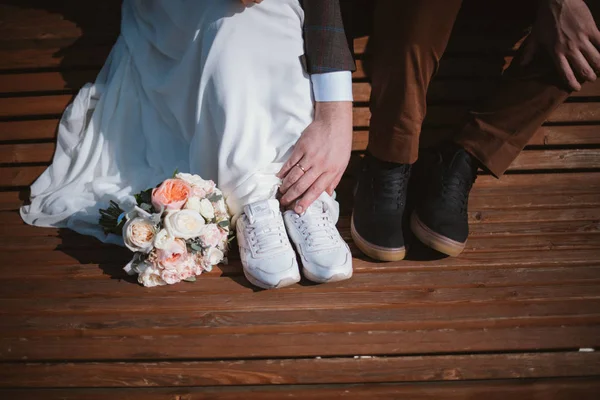 Lábak a menyasszony és a vőlegény a fehér cipők és a menyasszonyi csokor — Stock Fotó