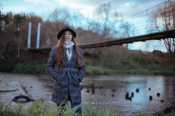 Девушка стоит на берегу реки у моста на облачном — стоковое фото