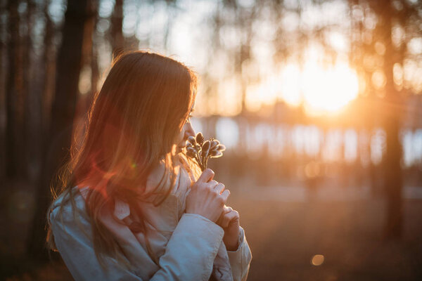 Portrait of a girl with willow branches in early spring at sunset. Close-up. Young woman in the setting sun outdoors with a blossoming willow