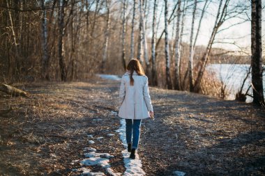 Bir kız son karda bir orman izi boyunca yürür.