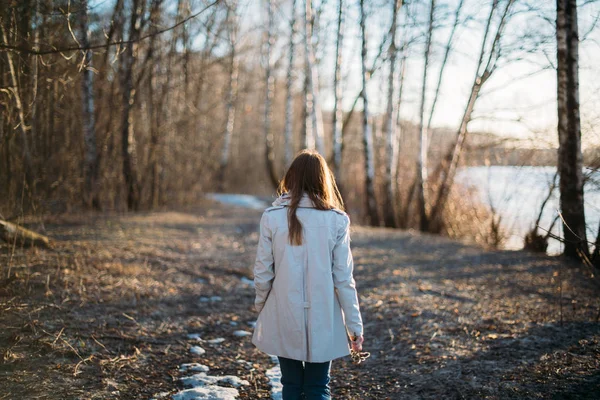 Uma menina caminha ao longo de uma trilha florestal através da última neve . — Fotografia de Stock