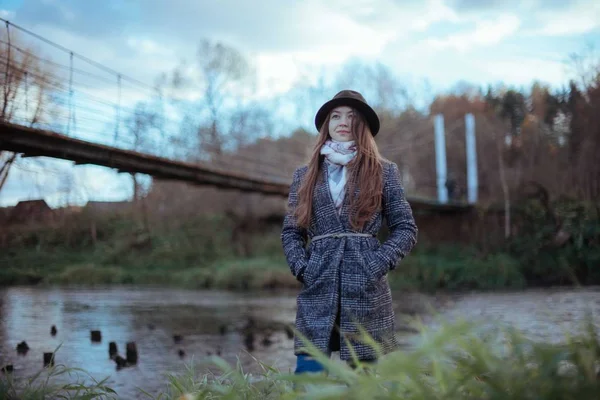 Una chica se para en la orilla del río en el puente en una nube —  Fotos de Stock