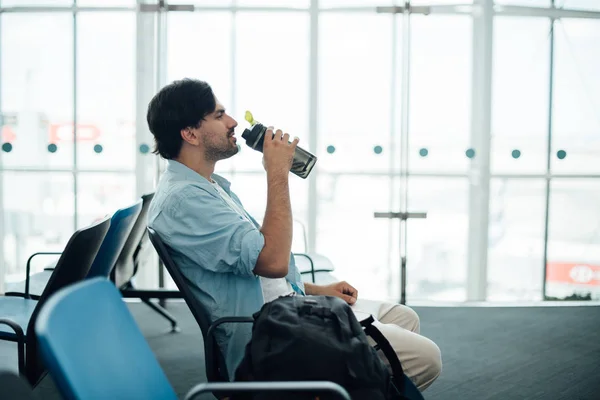 De man op de luchthaven te wachten voor vertrek, drinkwater. — Stockfoto