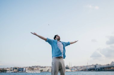 Rıhtımda denizin yanında genç bir adam sevinir ve güler.