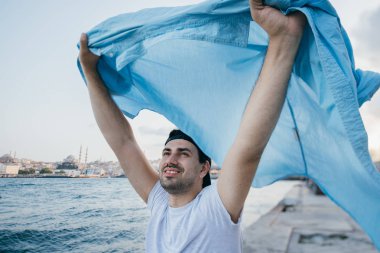 Rıhtımda denizin yanında genç bir adam sevinir ve güler.