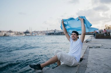 Rıhtımda denizin yanında genç bir adam sevinir ve güler.