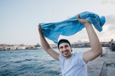 Rıhtımda denizin yanında genç bir adam sevinir ve güler.