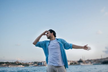 Rıhtımda denizin yanında genç bir adam sevinir ve güler.