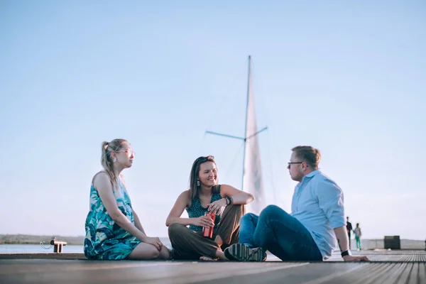 Een groep vrienden zitten op de pier en praten — Stockfoto