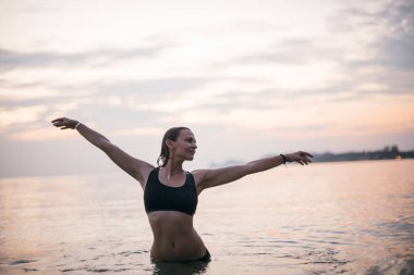 Bir kadın akşamdan ve gün batımında okyanustan zevk alır. Tropik bir adada, okyanusun sakin sularında poz veren genç bir kız. Tropik bölgelerde tatiller