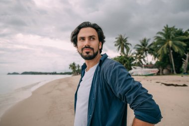 Yalnız bir adam bulutlu bir günde palmiye ağaçlarıyla kumsalda yürüyor. Genç yakışıklı adam bulutlu bir havada okyanusun kenarında kumda tek başına yürüyor..