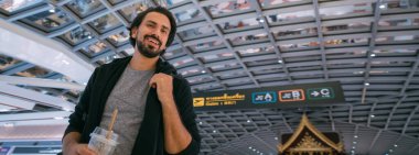 Havaalanında sırt çantalı genç bir adam. Neşeli adam terminalde yürüyor, uçağın uçmasını bekliyor.