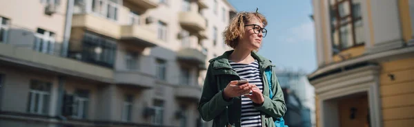 A woman with a phone goes on a European street. A young girl communicates online, looks for a way in the navigator, walks around the city on a sunny day