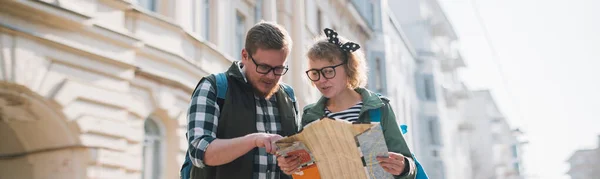 一对夫妇的游客在一个欧洲城市与地图 一个拿着旅游地图的男女青年正沿着欧洲的街道走着 在纸质地图上找到旅行路线 — 图库照片