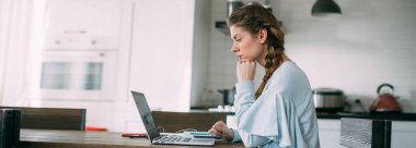 Bir kadın oturma odasında dizüstü bilgisayarla oturuyor, ekrana bakıyor, notlar alıyor, internetten yabancı bir dil öğreniyor, online eğitim kursları okuyor, internetten eğitim alıyor, bir müşteriye danışmanlık yapıyor.