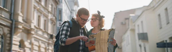 A couple of tourists in a European city with a map. A young man and woman with a tourist map in their hands are walking along European streets. Finding a travel route on a paper map