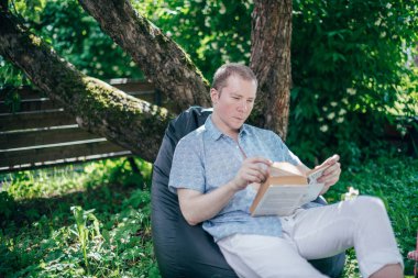 Bahçede bir adam dinleniyor ve bir sedirin üzerinde kitap okuyor. İzin günü ve dinlenme. Genç bir adam, güneşli bir günde elinde kitapla bir kır evinin gölgesinde bir ağacın altında yatıyor.