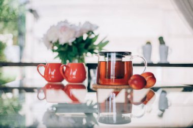 Çay aksesuarları ve çiçeklerle dolu bir hayat. Çaydanlık, çay fincanları ve parlak bir günde cam bir masanın üzerinde şakayık demeti