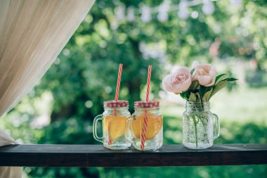İçkileri ve çiçekleri tazeleyen bir hayat. Gözlüklü bardaklar ve limonata ve limonata dilimli pipetler. Aydınlık bir günde bahçenin arka planında şakayık demeti