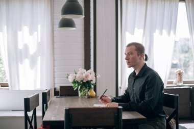 Genç bir adam masadaki bir deftere yazar. Gazeteci, yazar notlar alır, işyerindeki yazılar üzerinde çalışır.