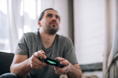 Adam kanepede video oyunu oynuyor. Elinde kumanda kolu olan genç bir adam konsolda hevesle oyun oynuyor.