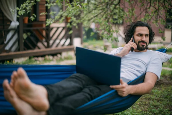 Een Man Werkt Met Een Laptop Smartphone Een Hangmat Een — Stockfoto