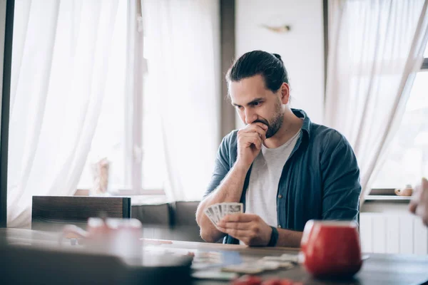 Friends play a board game in the living room. The company of young guys sits at a table and emotionally and cheerfully plays a card game on the weekend