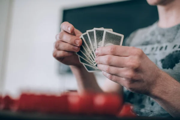 Friends play a board game in the living room. The company of young guys sits at a table and emotionally and cheerfully plays a card game on the weekend. Hands with cards close-up