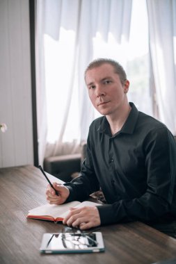 Genç bir adam masadaki bir deftere yazar. Gazeteci, yazar notlar alır, işyerindeki yazılar üzerinde çalışır.