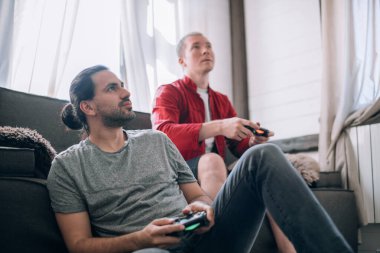 Çocuklar kanepede video oyunu oynuyorlar. Elinde joysticklerle iki genç adam büyük bir hevesle bir konsolda oyun oynuyorlar.