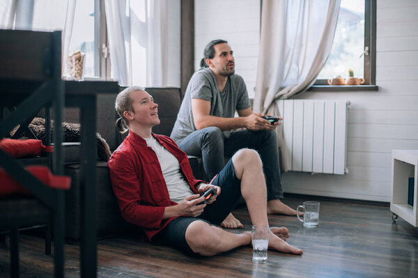 Ребята играют в видеоигры на диване. Два молодых человека с джойстиками в руках с энтузиазмом играют в игру на консоли