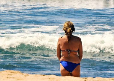 Mavi bikinili kadın denize bakıyor.