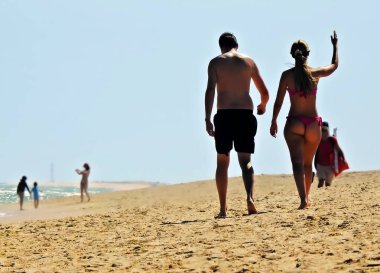 Sahilde kumda yürüyen bir erkek ve bir kız.