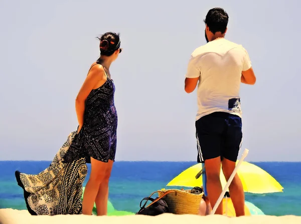 Mavi denizin kıyısından uzağa bakan bir çift.