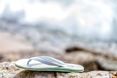 Bulanık arka planda kayalık bir plajda kayıp beyaz bir plaj terliği.