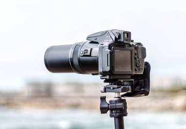 Ön planda bulanık arkaplanı olan bir tripodun üzerindeki kamera.