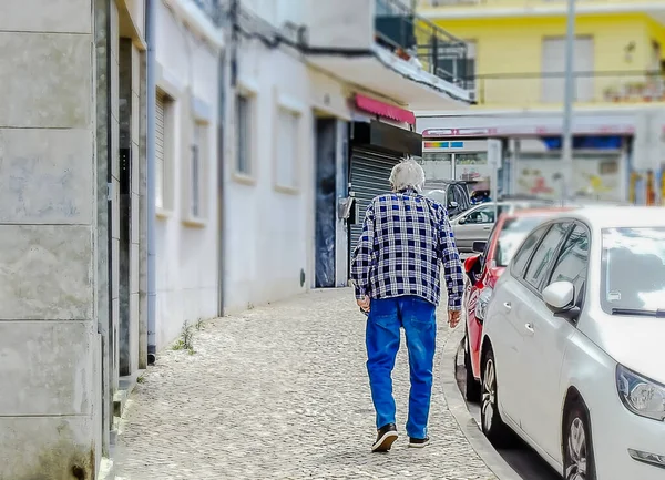 An old man walking down a city street among cars