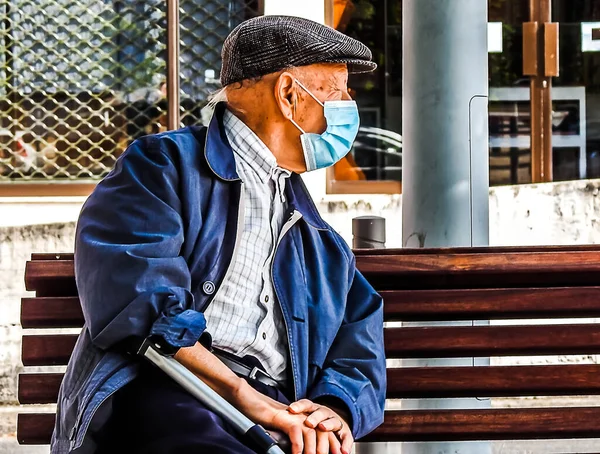 An old man with a protective mask sitting on a bench