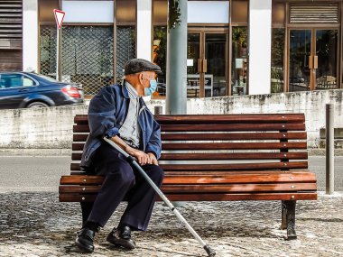 Yaşlı bir adam salgın sırasında bankta oturuyor ve maske takıyor.