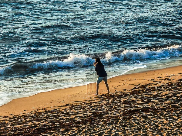 A woman in a gray blouse playing on the beach near the ocean water at sunset