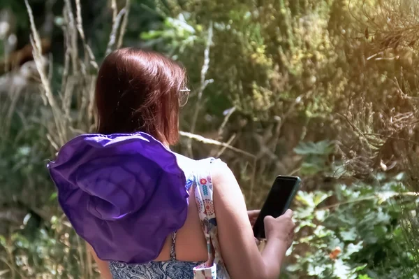 Ormanda sırt çantası ve cep telefonu olan bir kadın..