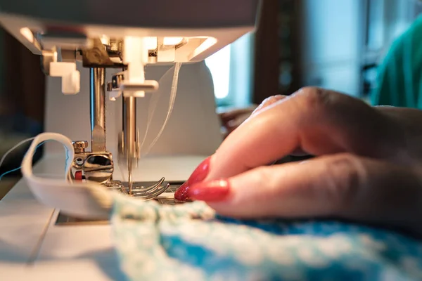 Las manos femeninas cosen una máscara protectora utilizando una moderna máquina de coser eléctrica. Concepto de seguridad durante una epidemia viral . —  Fotos de Stock