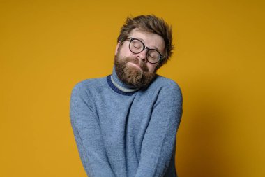 Tüylü saçlı, sakallı, utangaç beyaz bir adam. Alçak gönüllü, katlanmış elleri ve kapalı gözleri var. Yüzünde sevimli bir ifade var..