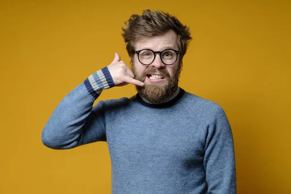 Un hipster insatisfecho y nervioso hace un gesto telefónico con los dedos y mira a la cámara. Llámenme. Lenguaje corporal . — Foto de Stock