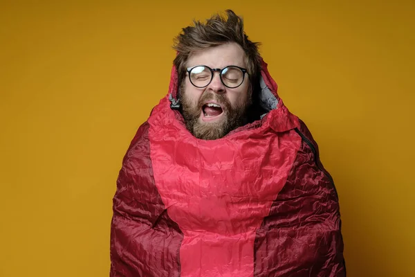 Funny, yawning man in a sleeping bag on a yellow background, he sleeps and imaginary himself in a wonderful travel. — Stock Photo, Image